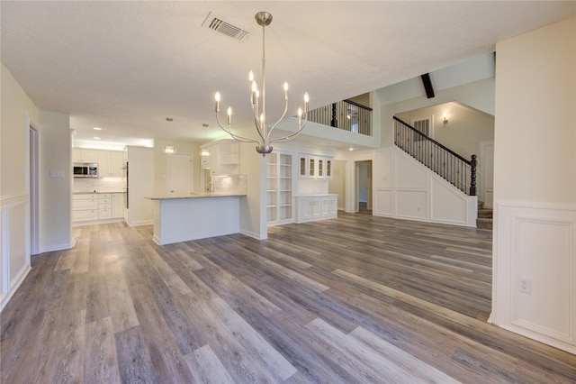 unfurnished living room with a chandelier, wood finished floors, a wainscoted wall, a decorative wall, and stairway