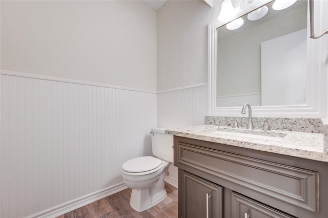 half bathroom with wood finished floors, toilet, a wainscoted wall, and vanity