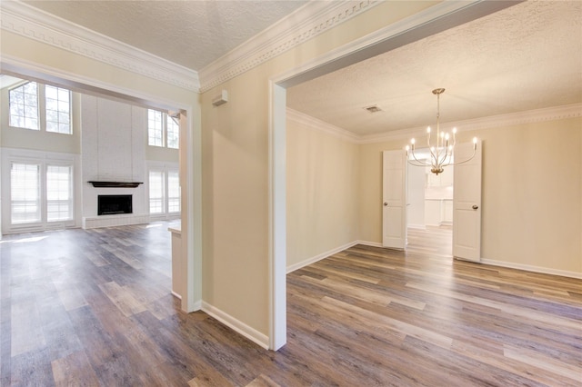 spare room with a chandelier, wood finished floors, a textured ceiling, a large fireplace, and crown molding