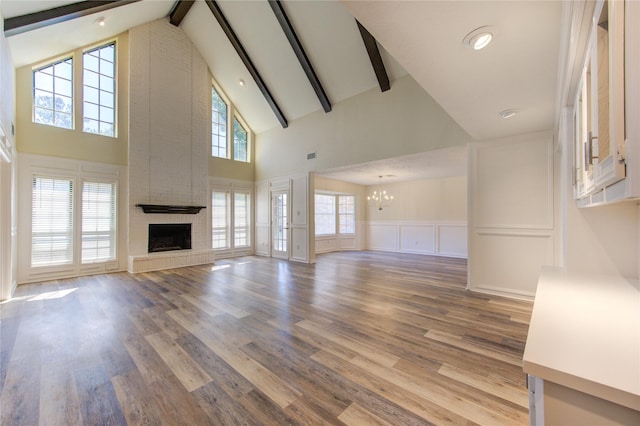 unfurnished living room featuring a chandelier, a fireplace, high vaulted ceiling, wood finished floors, and beamed ceiling