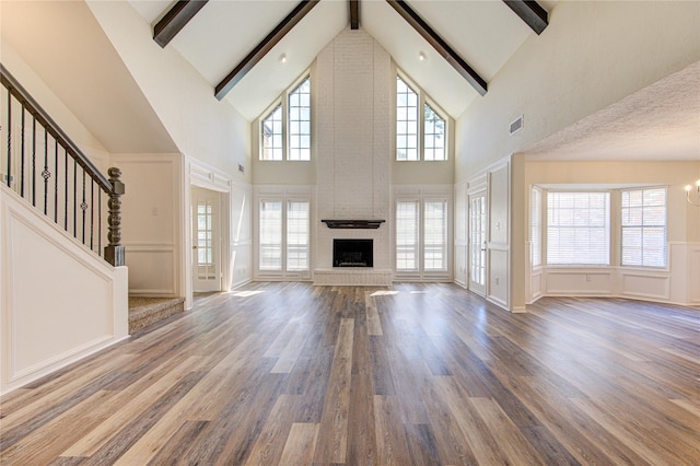 unfurnished living room featuring beamed ceiling, high vaulted ceiling, a chandelier, a fireplace, and a decorative wall