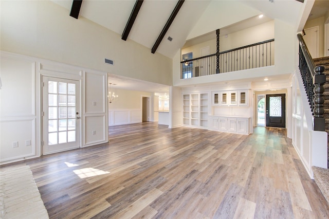 unfurnished living room featuring high vaulted ceiling, a chandelier, a decorative wall, light wood-style flooring, and beam ceiling