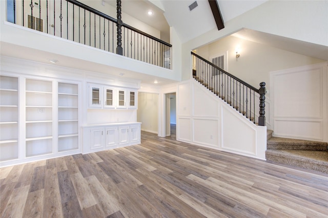 unfurnished living room with wood finished floors, high vaulted ceiling, stairway, beam ceiling, and recessed lighting