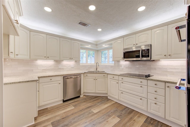 kitchen featuring appliances with stainless steel finishes, a sink, a textured ceiling, light wood-type flooring, and light stone countertops