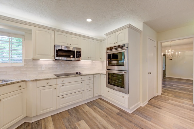 kitchen with appliances with stainless steel finishes, a chandelier, light wood-style floors, a textured ceiling, and decorative backsplash