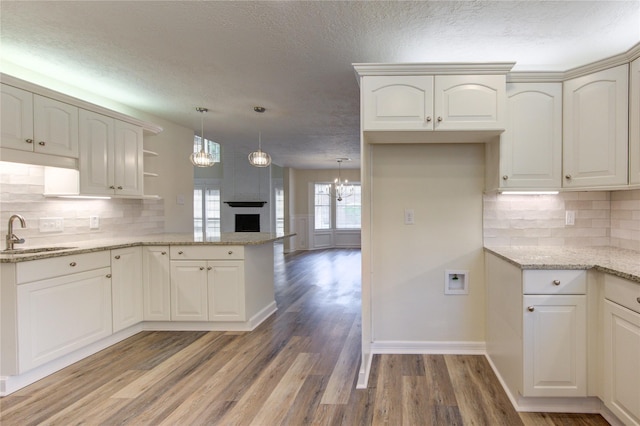 kitchen featuring a sink, a peninsula, light wood-type flooring, a textured ceiling, and a chandelier