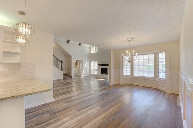 unfurnished dining area featuring a textured ceiling, a chandelier, wood finished floors, stairway, and a decorative wall