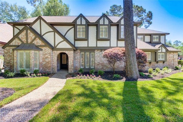 tudor house with stucco siding, a front yard, and brick siding