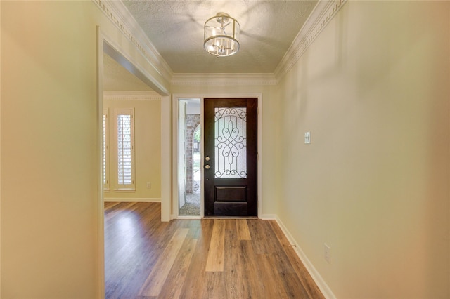 entrance foyer featuring wood finished floors, a chandelier, a textured ceiling, baseboards, and crown molding