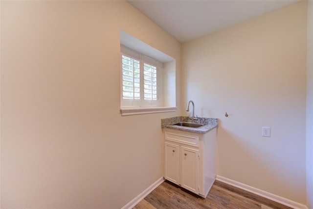 clothes washing area featuring a sink, wood finished floors, and baseboards