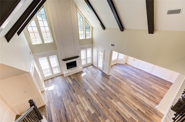 unfurnished living room with high vaulted ceiling, wood finished floors, beamed ceiling, and a brick fireplace