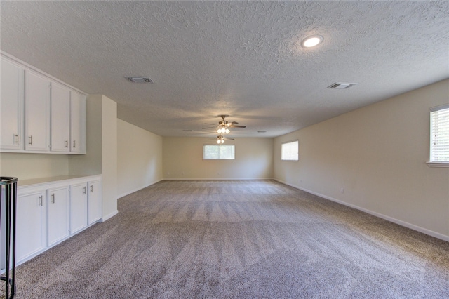 spare room with a textured ceiling, light colored carpet, ceiling fan, and baseboards