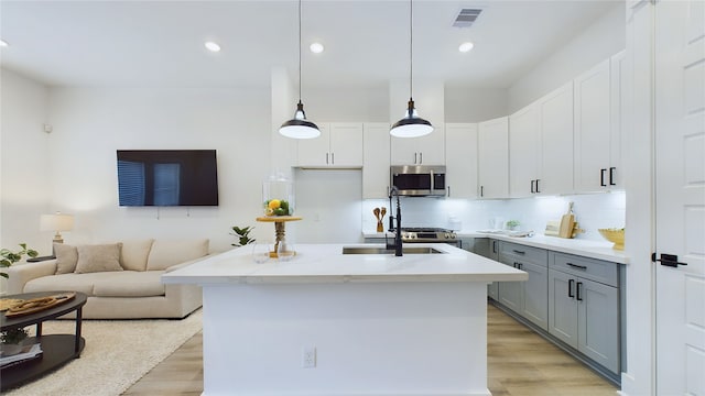 3019 Jensen Springs Ln, Houston, TX 77026 - kitchen with stainless steel microwave, gray cabinets, light wood-type flooring, decorative backsplash, and a center island with sink