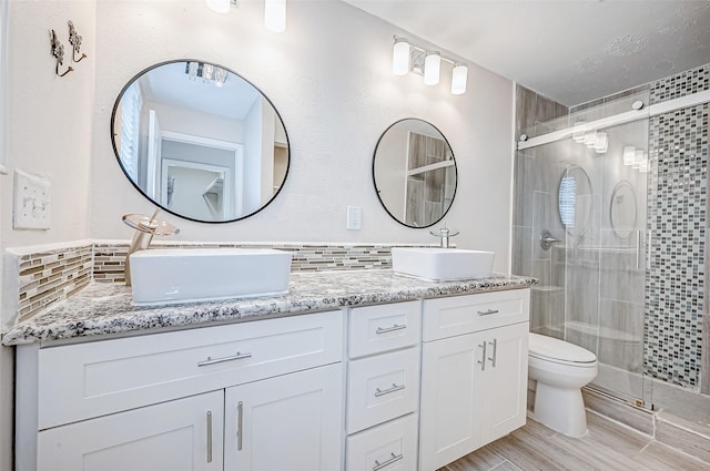full bathroom featuring a shower stall, toilet, double vanity, and backsplash