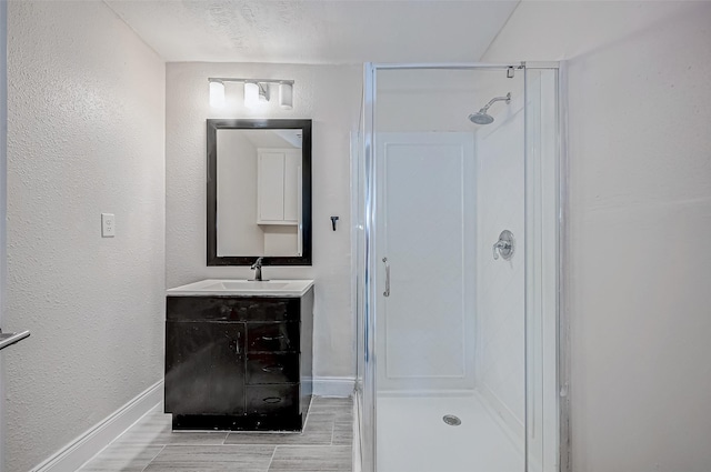 full bath with a stall shower, baseboards, vanity, and a textured wall