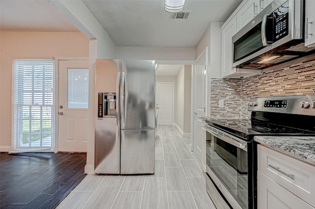 kitchen with stainless steel appliances, decorative backsplash, baseboards, white cabinetry, and light wood finished floors