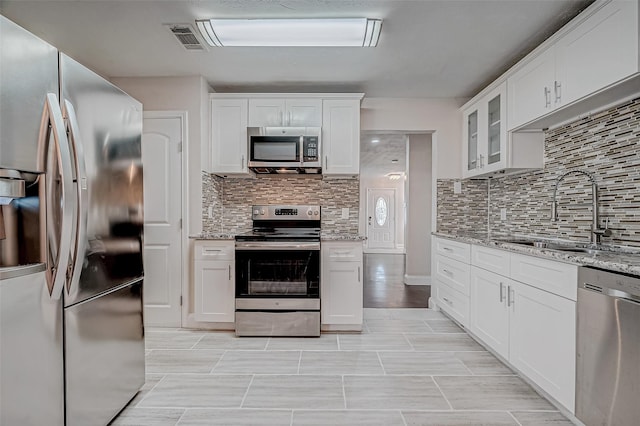 kitchen with stainless steel appliances, a sink, backsplash, and white cabinets