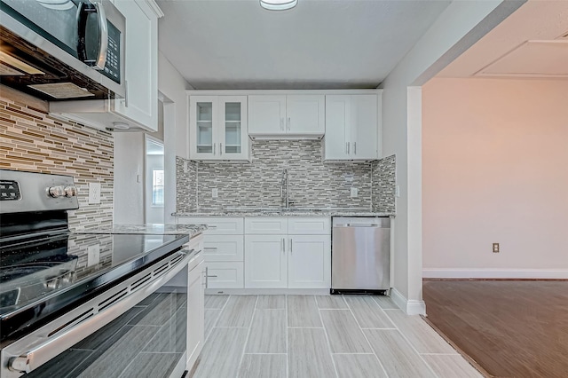 kitchen with stainless steel appliances, a sink, light stone counters, white cabinets, and decorative backsplash