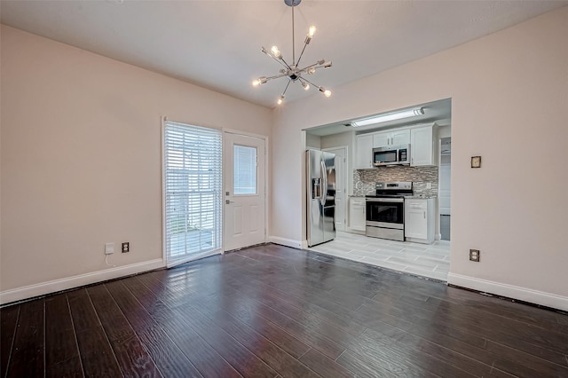 unfurnished living room with a chandelier, baseboards, and wood finished floors