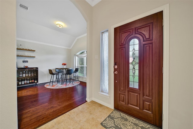 foyer with crown molding, vaulted ceiling, arched walkways, healthy amount of natural light, and baseboards