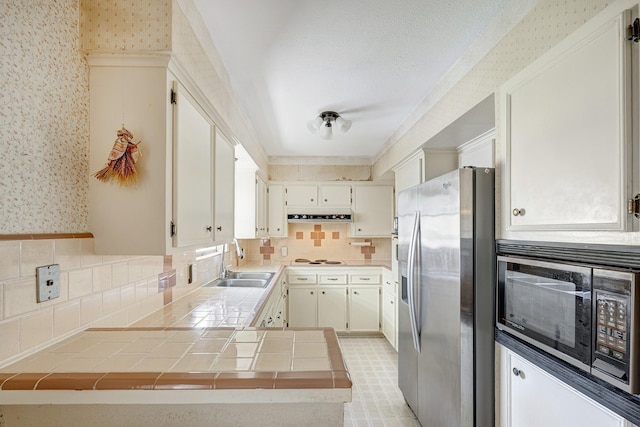 9603 Emnora Ln, Houston, TX 77080 - kitchen featuring appliances with stainless steel finishes, wallpapered walls, a sink, tile counters, and a peninsula