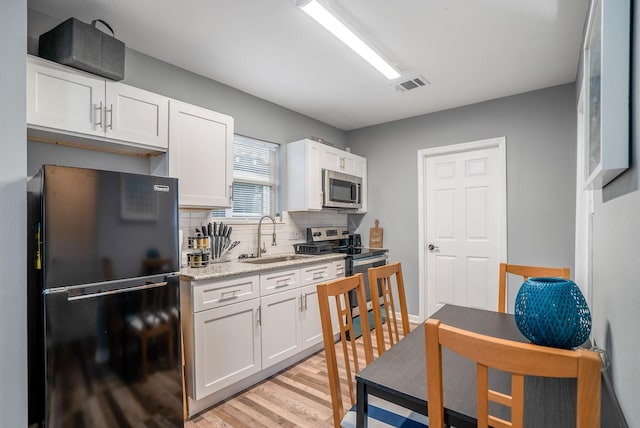 3409 Providence St, Houston, TX 77020 - kitchen with stainless steel appliances, a sink, white cabinetry, tasteful backsplash, and light wood-style flooring