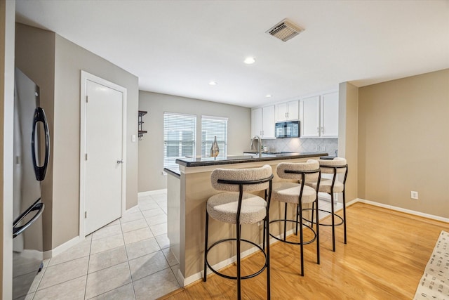 1244 W 18th St, Houston, TX 77008 - kitchen featuring black microwave, freestanding refrigerator, dark countertops, a kitchen breakfast bar, and backsplash