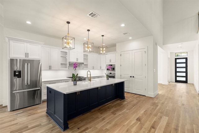 1038 W 31st St, Houston, TX 77018 - kitchen featuring appliances with stainless steel finishes, white cabinets, light wood finished floors, light countertops, and a large island with sink