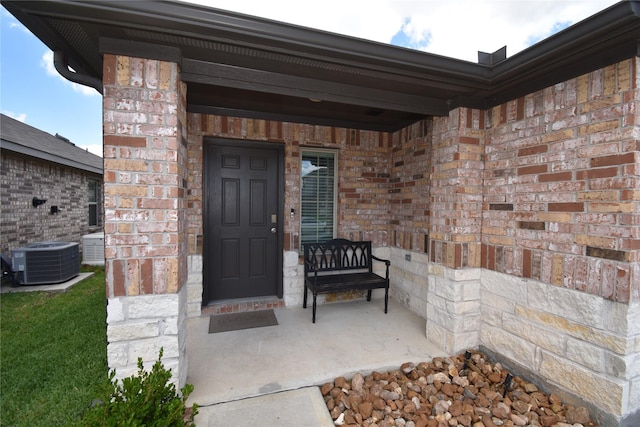 view of exterior entry with central AC, covered porch, and brick siding