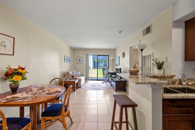 13151 Walden Rd Unit 135, Montgomery, TX 77356 - kitchen featuring a textured wall, a breakfast bar area, open floor plan, light stone countertops, and light tile patterned flooring
