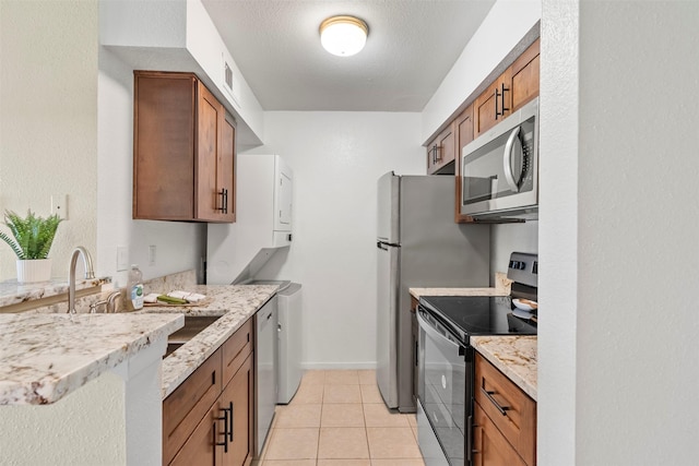 13151 Walden Rd Unit 135, Montgomery, TX 77356 - kitchen featuring appliances with stainless steel finishes, brown cabinetry, light tile patterned floors, and light stone countertops