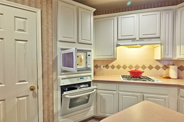 kitchen featuring white appliances, under cabinet range hood, light countertops, wallpapered walls, and white cabinets