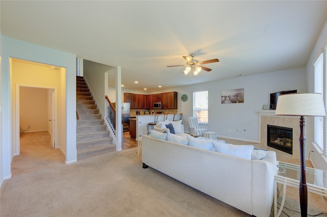 living area with a ceiling fan, a tiled fireplace, stairs, baseboards, and recessed lighting