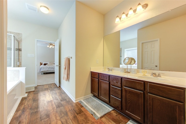 bathroom with wood finished floors, a stall shower, double vanity, a garden tub, and connected bathroom