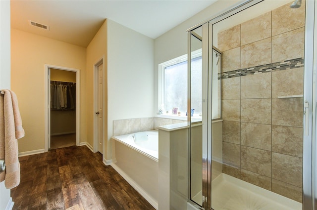 bathroom with a stall shower, wood finished floors, a bath, and a walk in closet