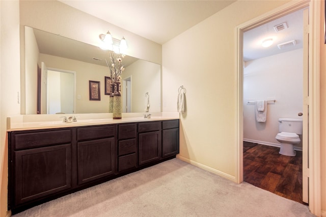 bathroom with baseboards, double vanity, and toilet