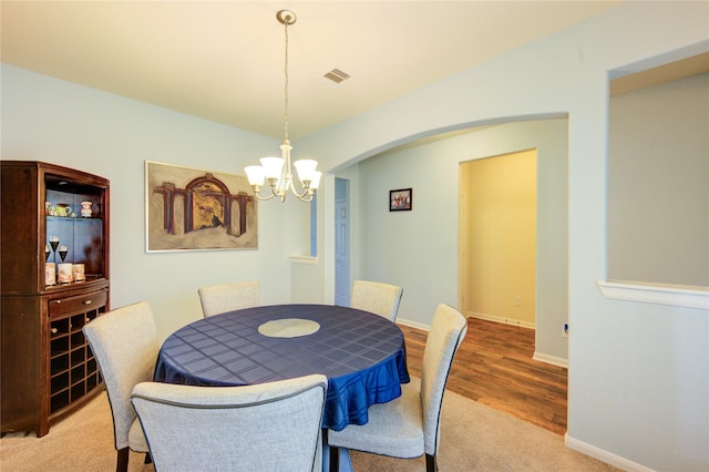 carpeted dining space featuring a chandelier, arched walkways, baseboards, and wood finished floors