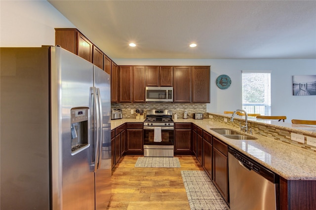 kitchen featuring appliances with stainless steel finishes, a sink, light wood finished floors, decorative backsplash, and a peninsula