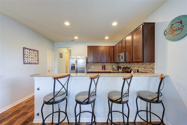 kitchen featuring appliances with stainless steel finishes, a peninsula, backsplash, recessed lighting, and dark wood-type flooring