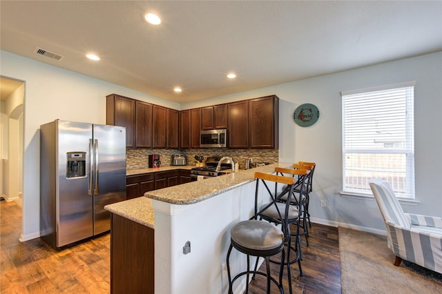 kitchen with stainless steel appliances, a peninsula, a breakfast bar, dark wood-style flooring, and recessed lighting