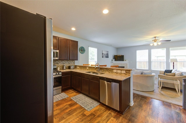 kitchen featuring appliances with stainless steel finishes, a sink, open floor plan, a peninsula, and dark wood-style flooring