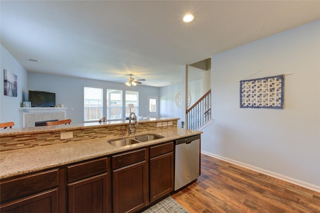 kitchen with stainless steel dishwasher, a sink, dark wood-type flooring, open floor plan, and a tile fireplace