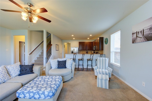 living area with a ceiling fan, recessed lighting, baseboards, stairs, and light colored carpet