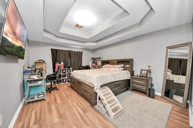 bedroom featuring a raised ceiling, wood finished floors, baseboards, and a desk