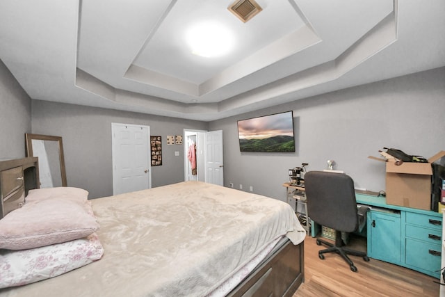 bedroom with a raised ceiling, light wood-style flooring, and an office area