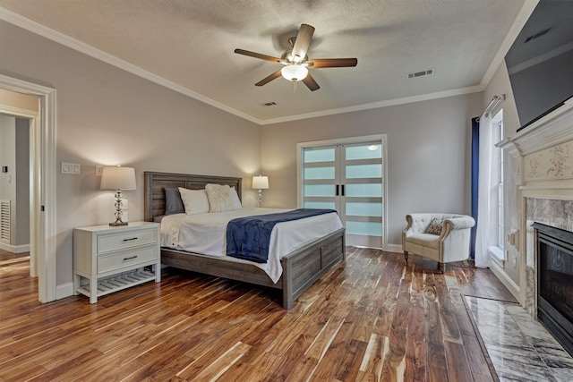bedroom with hardwood / wood-style floors, a tile fireplace, crown molding, baseboards, and ceiling fan