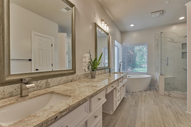 bathroom with a marble finish shower, double vanity, a soaking tub, wood finished floors, and recessed lighting