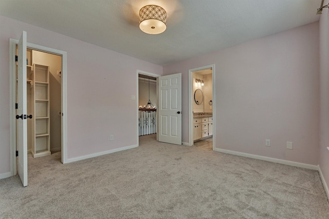 unfurnished bedroom with light colored carpet, baseboards, a spacious closet, and ensuite bath