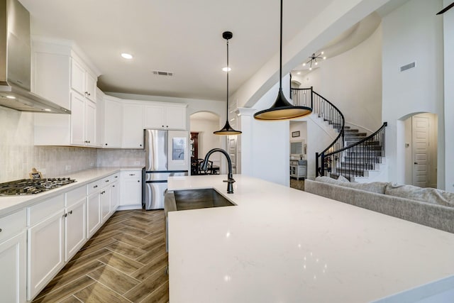12531 Tullich Run Dr, Humble, TX 77346 - kitchen with wall chimney exhaust hood, appliances with stainless steel finishes, arched walkways, a sink, and white cabinetry