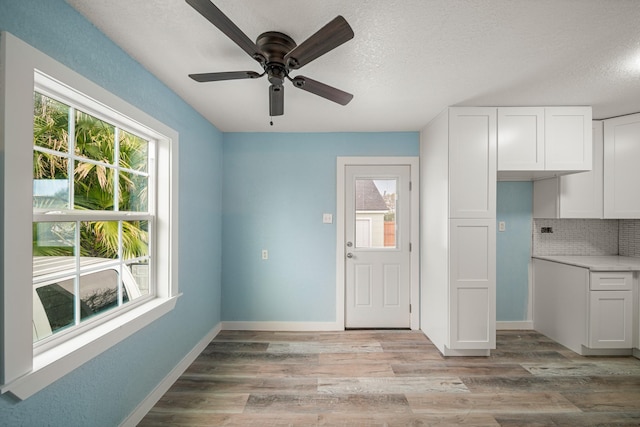 5528 Menard Ave, Galveston, TX 77551 - kitchen featuring white cabinets, tasteful backsplash, ceiling fan, and light wood-style flooring